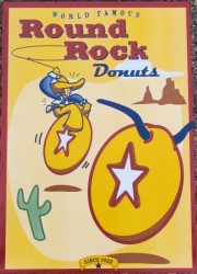 Image of Round Rock donut box. One donut has horns like a longhorn cow; a cowboy is riding the other donut and attempting to lasso the longhorn donut.