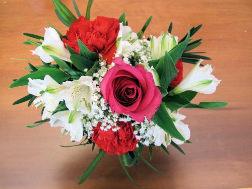 Flower arrangement of red carnations, white alstroemeria, baby's breath, and one red rose.